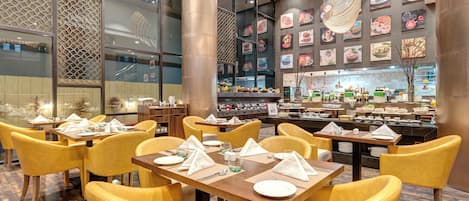 A restaurant with yellow chairs and tables, a buffet area, and a wall decorated with food images.