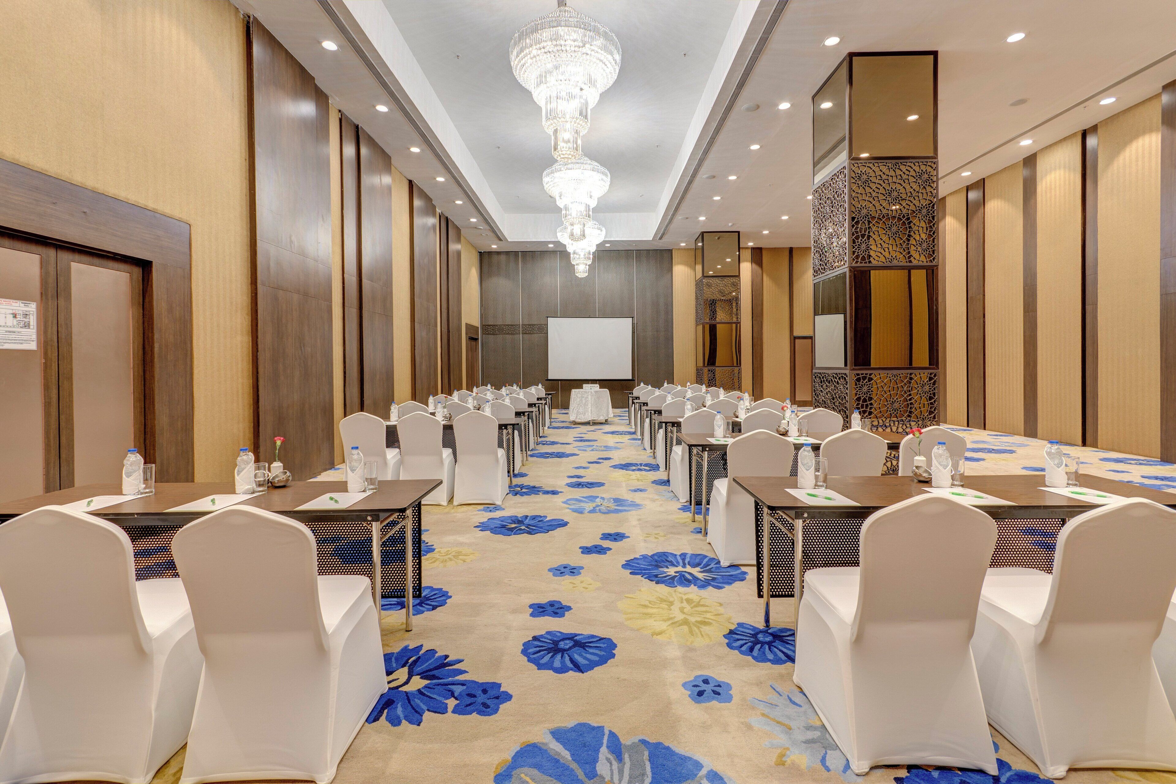 A conference room with rows of tables, chairs, and a large screen at the front.