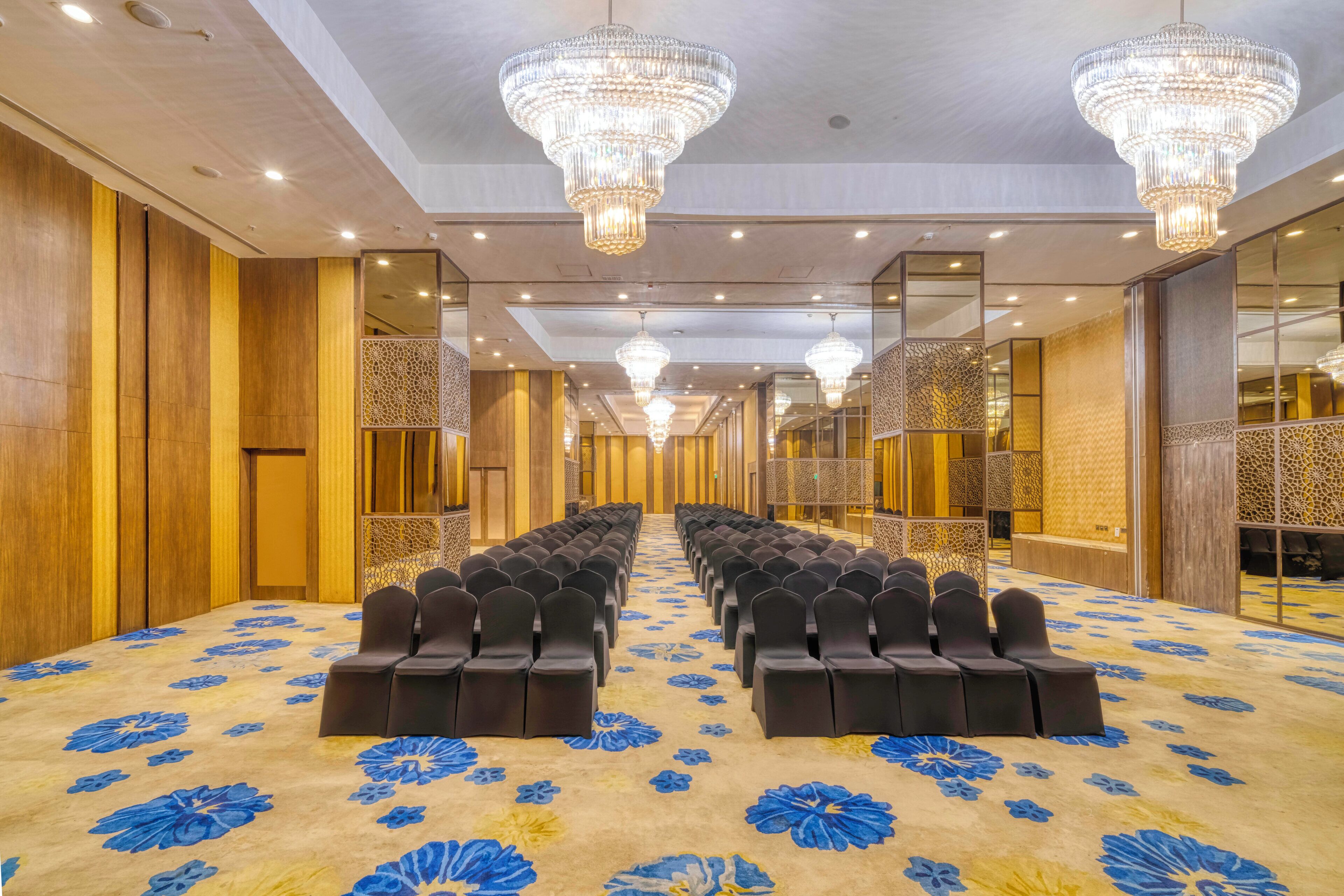 A hotel conference room with rows of chairs, chandeliers, and a patterned carpet.