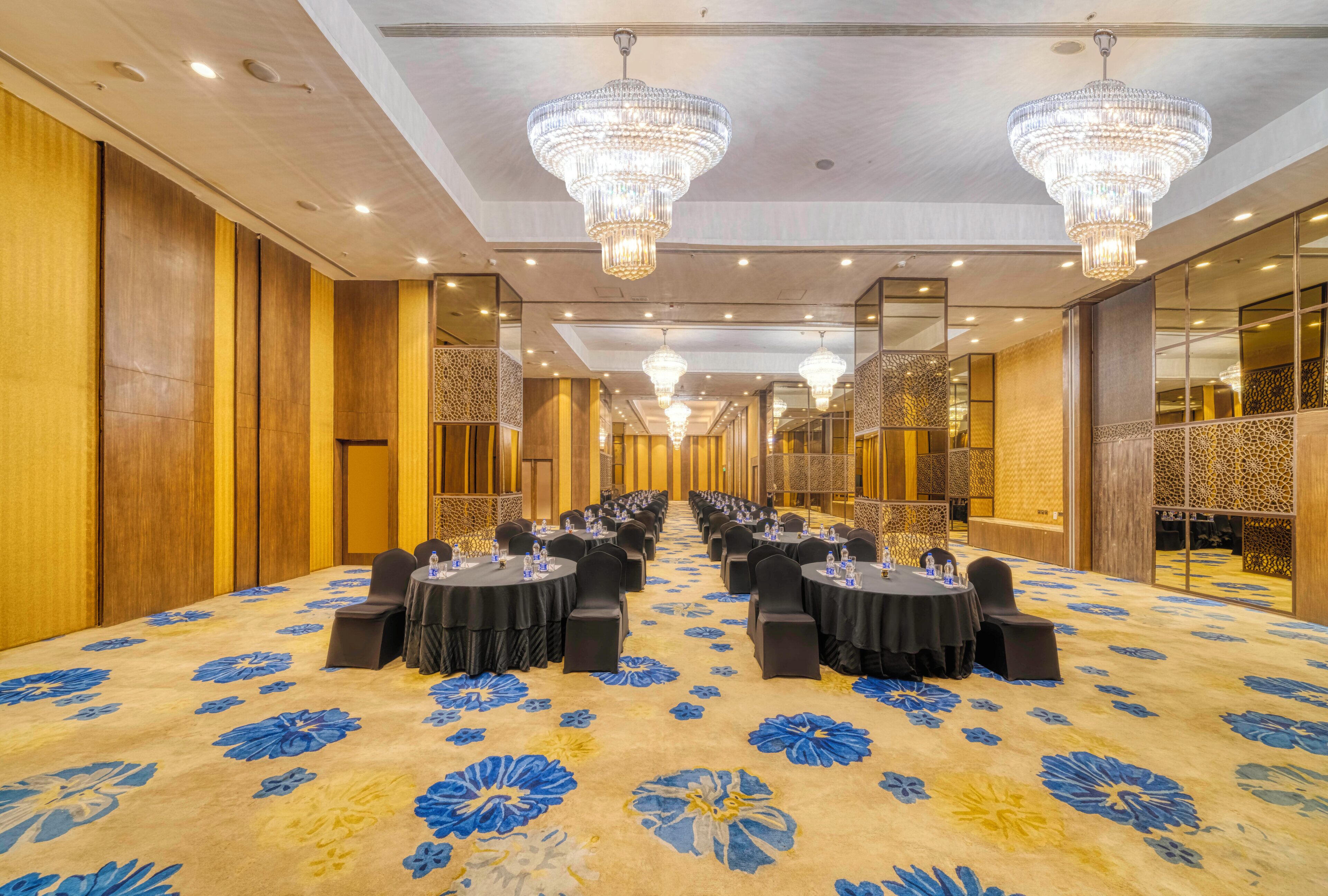 A hotel conference room with rows of tables, black chairs, and floral carpet.