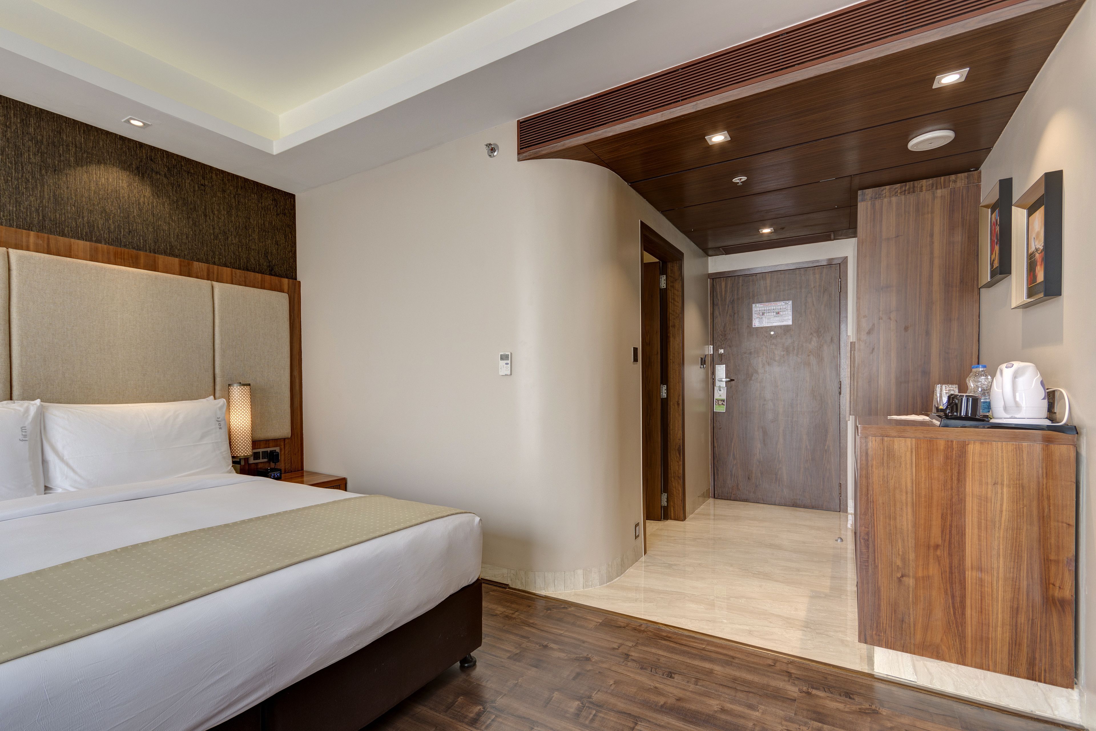 A hotel room with a bed, bedside table, and a wooden cabinet with a kettle.