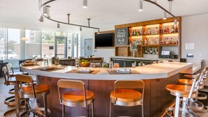 A modern bar area with a curved ceiling, bar stools, and a display of local brews. - Cambria Hotel LAX (El Segundo)