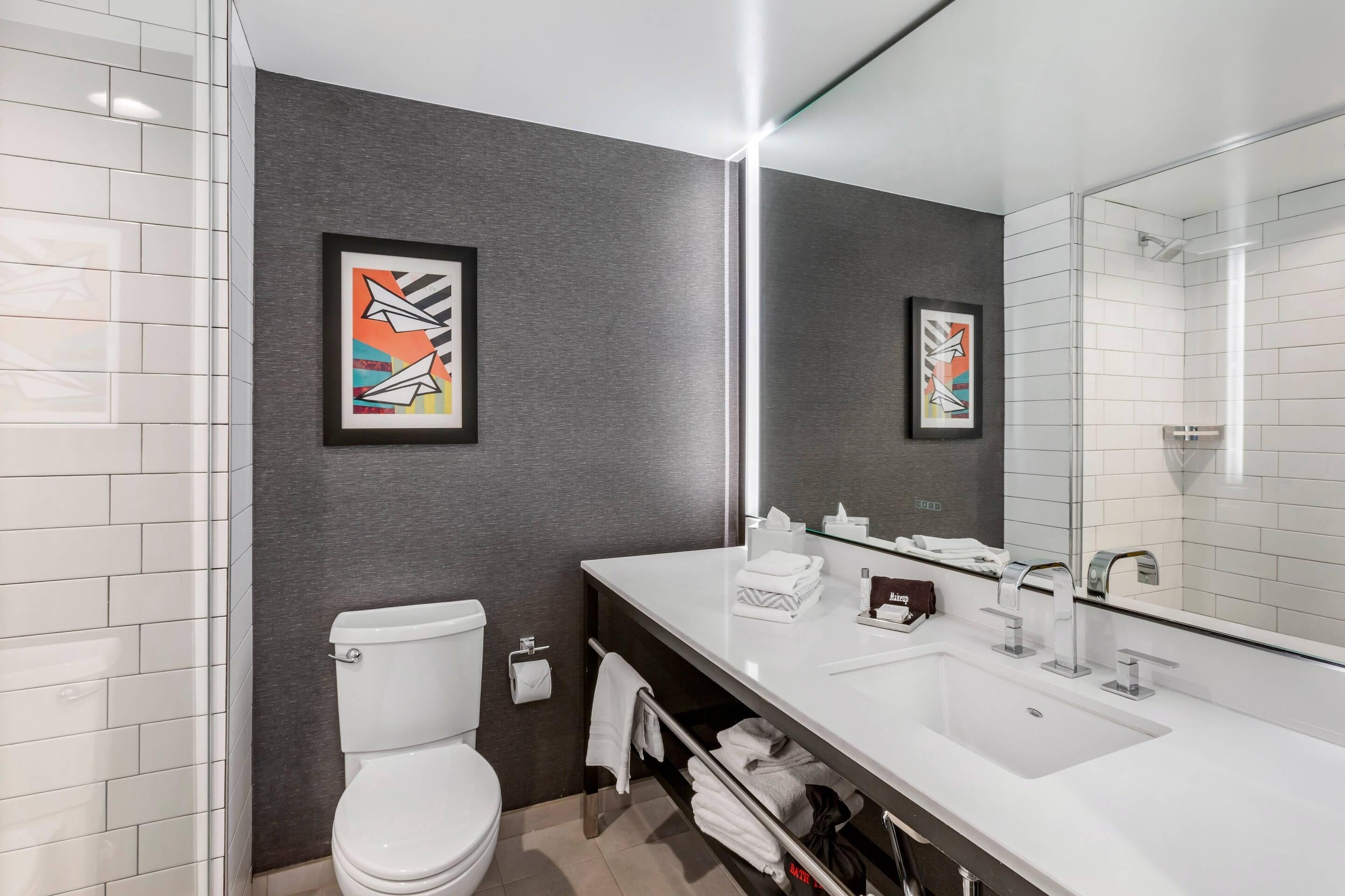 A modern bathroom with a white toilet, a large mirror, and a white sink.