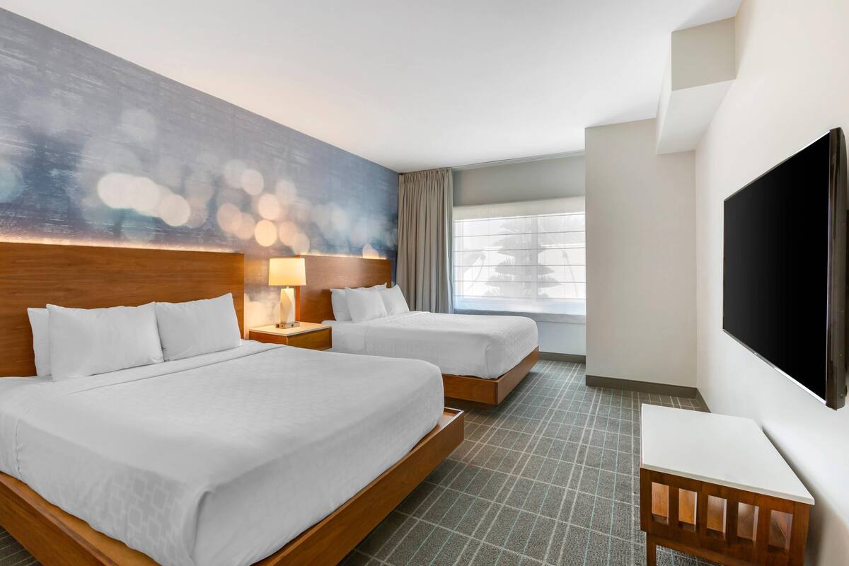 A hotel room with two beds, a TV, a painting, and a window with curtains.