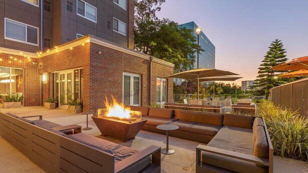 An outdoor patio area with a fire feature, seating, and a covered dining area. - Cambria Hotel LAX (El Segundo)