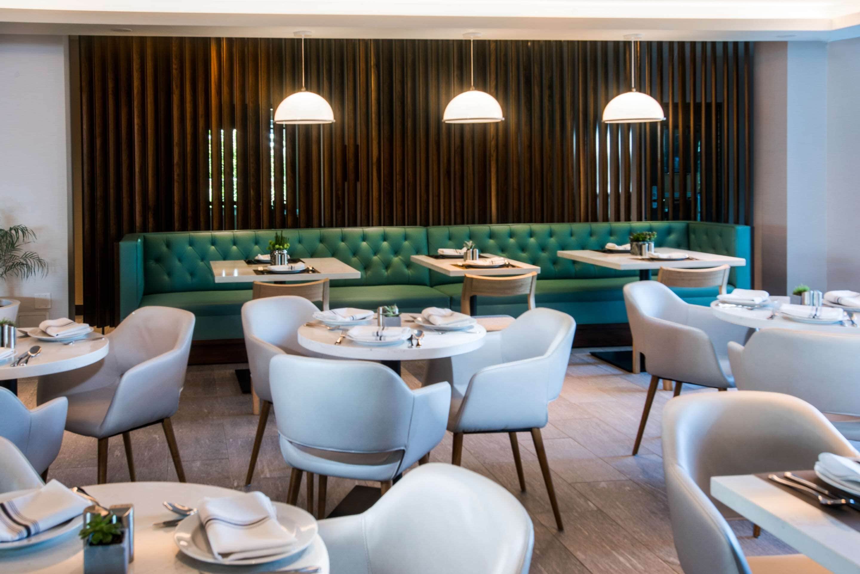 En modern restaurang med runda bord, vita stolar och en grön, klädd sittgrupp.