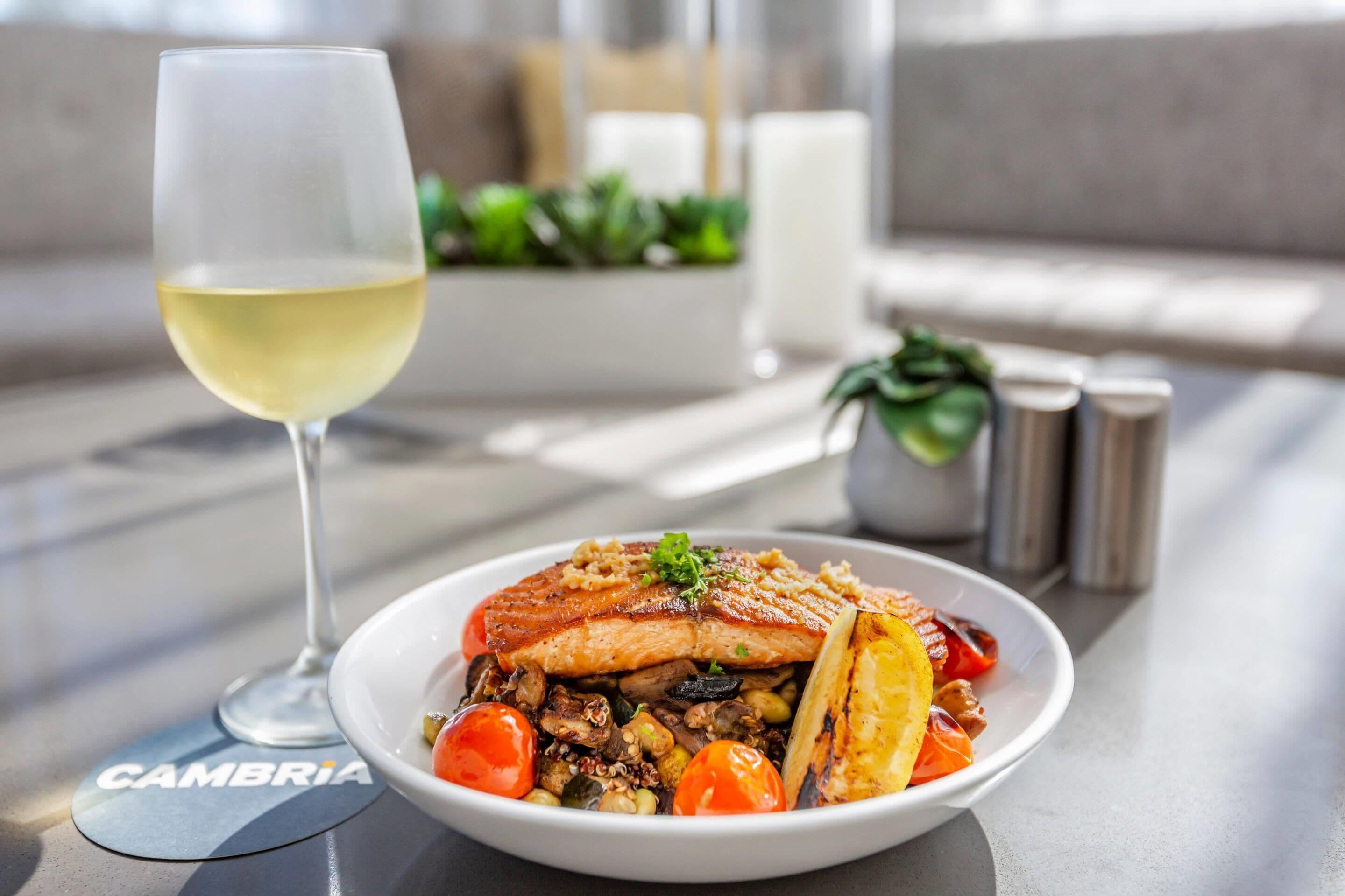 A meal with a glass of white wine on a table with a 'CAMBRIA' coaster.