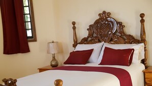 Una cama bien tendida con cabecera de madera, sábanas blancas y almohadas rojas.