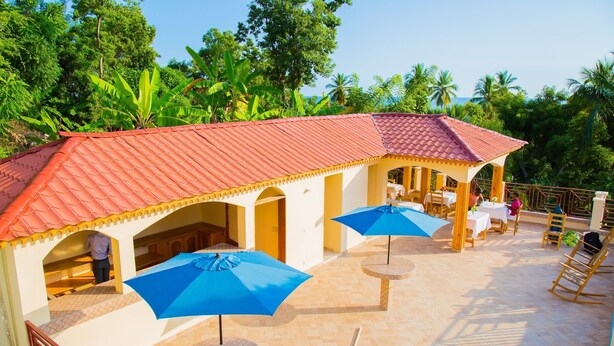 Un patio de hotel con mobiliario exterior, techo de tejas rojas y abundante vegetación al fondo.
