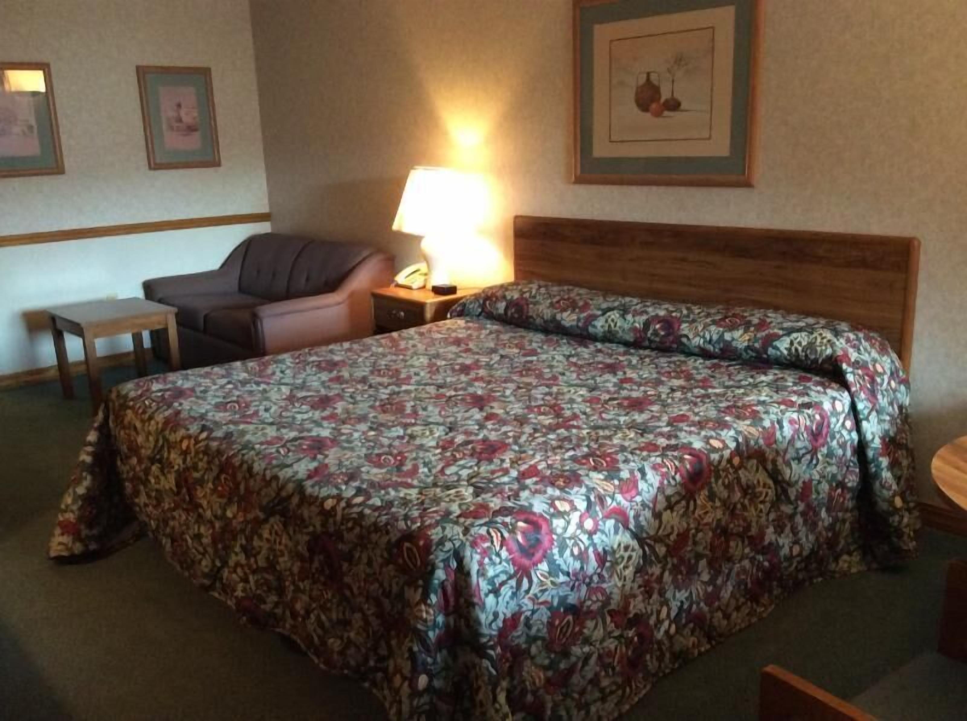 Habitación de hotel con una cama grande, una silla, una mesita y una mesita de noche con lámpara.