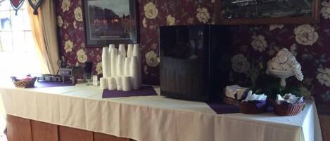 Habitación de hotel con una mesa lista para el desayuno, un televisor y papel tapiz con motivos florales.