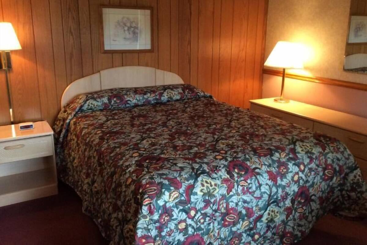 A bedroom with a bed, two bedside tables, a nightstand, a framed picture on the wall, and a lamp on each bedside table.