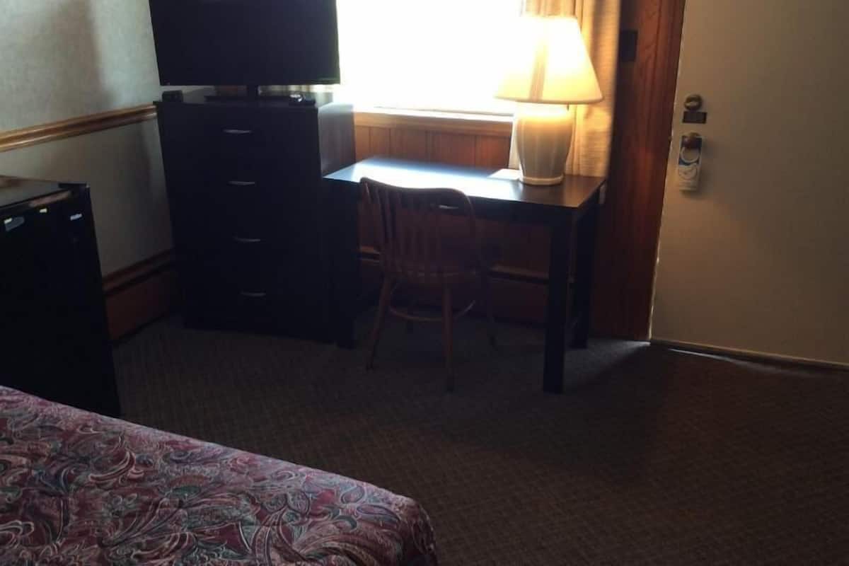 A hotel room with a bed, a desk with a chair, a television, and a lamp.