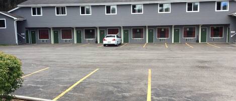 Un motel con una fila de habitaciones, un estacionamiento y un coche blanco estacionado al frente.