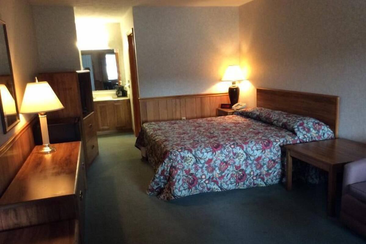 A hotel room with a bed, a desk, a chair, a lamp, and a mirror.