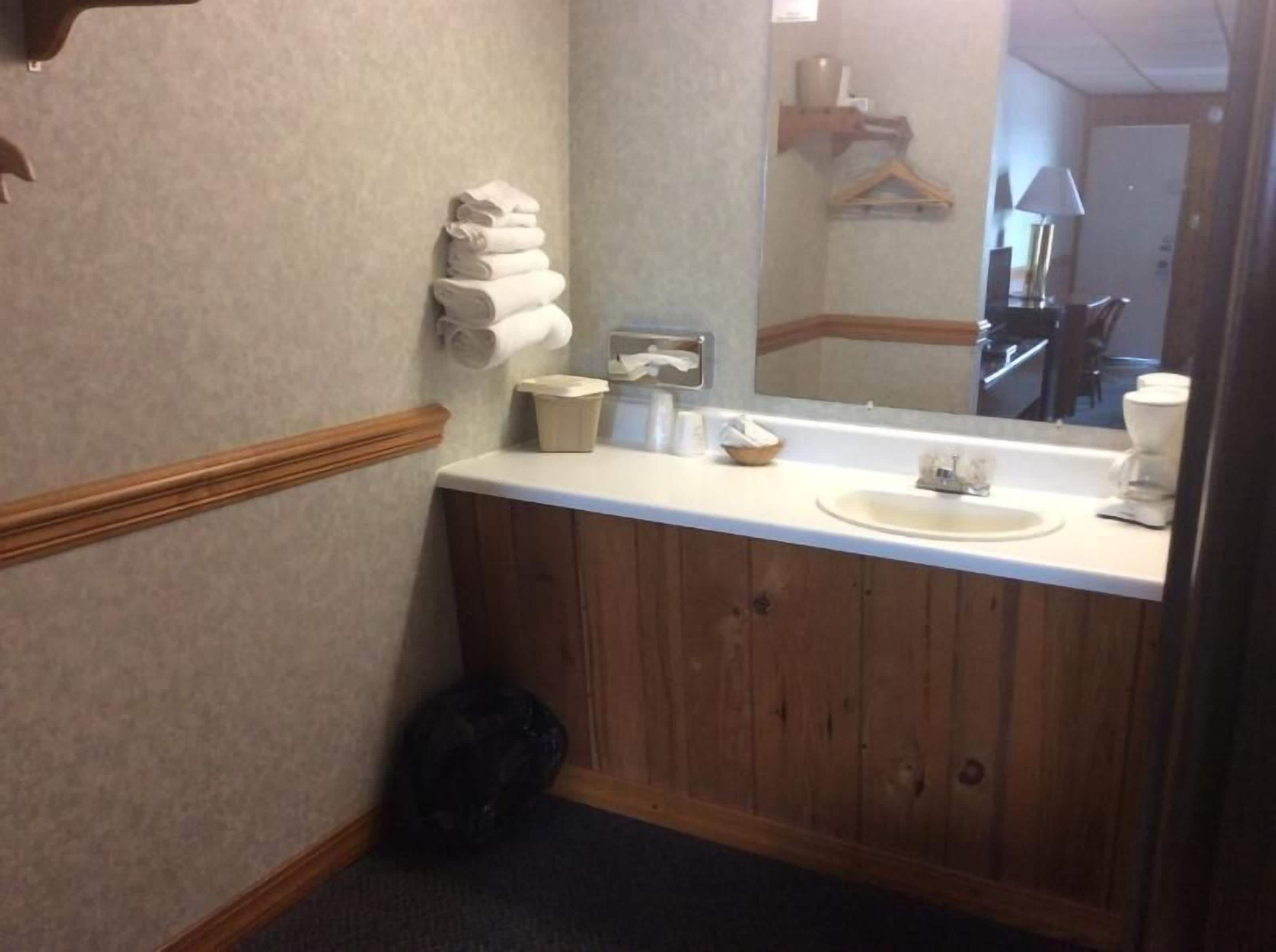 Un baño con un mueble de tocador de madera, un lavabo, un espejo y un perchero para toallas.