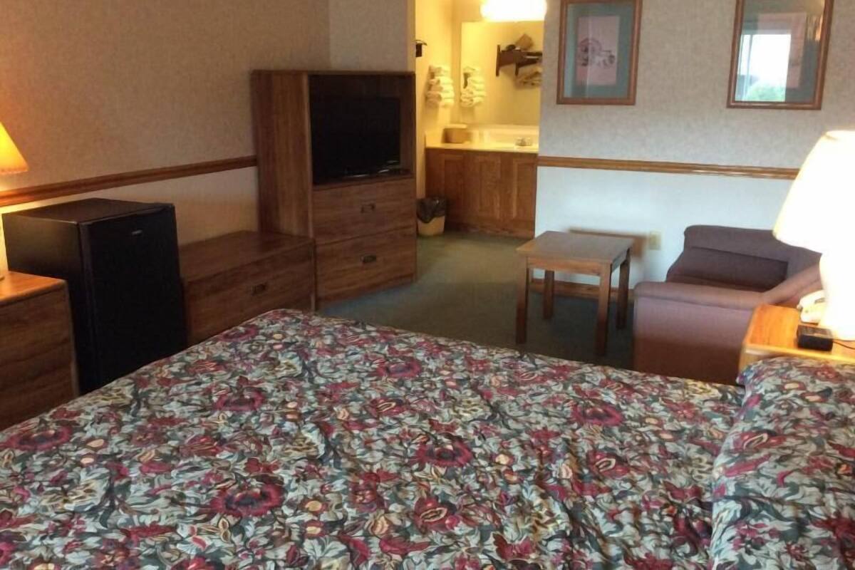 A hotel room with a bed, a desk, a chair, a television, and a small kitchenette.