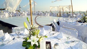 Montaje para una boda en la playa, con manteles blancos, centros de mesa florales y vista despejada al océano.