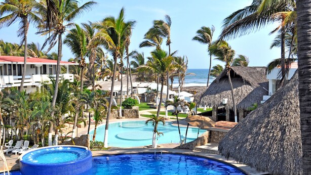 Un resort con una piscina grande rodeada de palmeras y chozas de techo de paja.