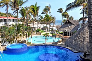 A resort with a large pool surrounded by palm trees and thatched-roof huts. - Mar Paraiso Queen (Acapulco)