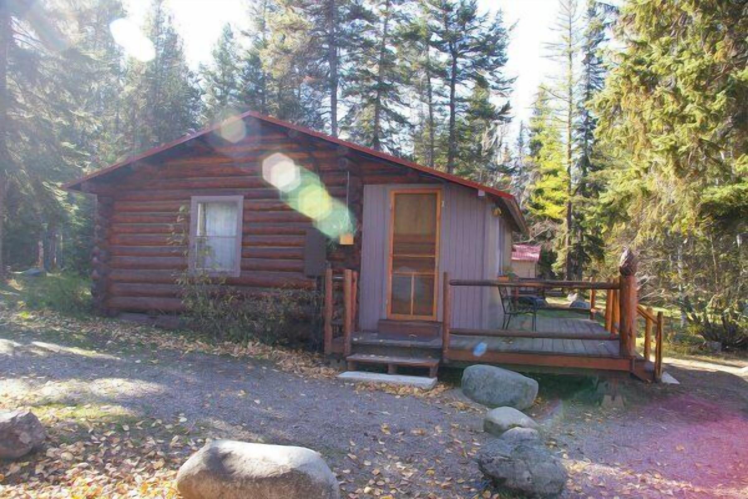 A log cabin with a wooden porch and a small deck.