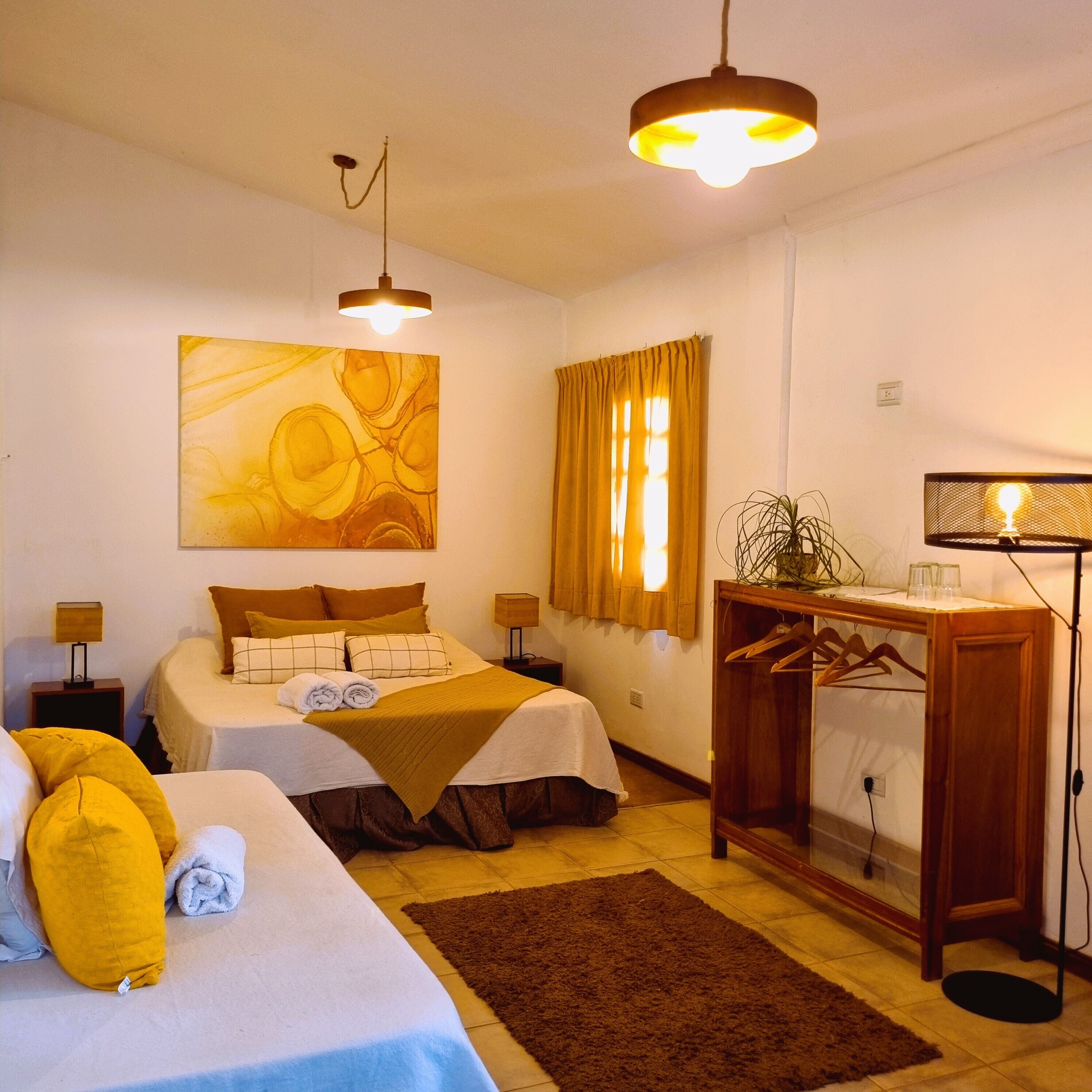 A hotel room with two beds, a large abstract painting, a plant, and a wooden dresser with a mirror.