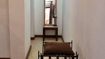 A narrow hallway with two black metal chairs with brown cushions, a wooden table with a mirror and books, and a brown rug on the floor.