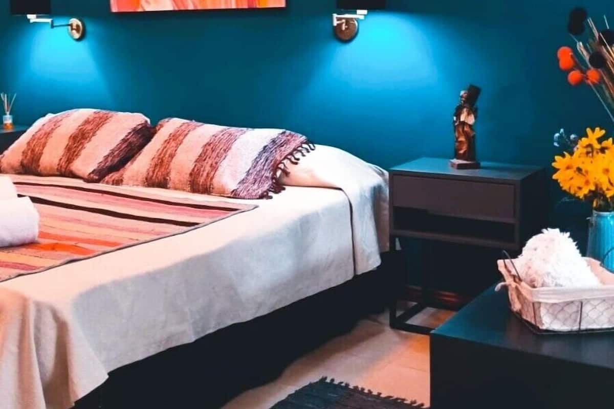 A bedroom with a bed, bedside tables, a nightstand, a wall-mounted lamp, and a painting.