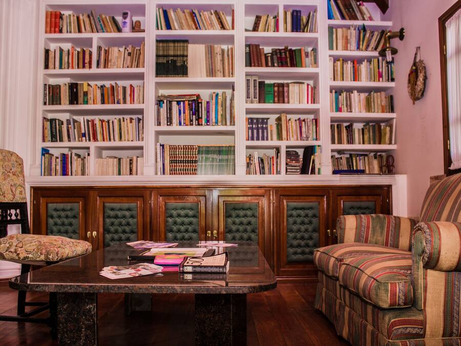 Un coin lecture confortable avec une cheminée, un canapé moelleux, une table basse en bois sur laquelle sont posés des livres, et une bibliothèque remplie d’ouvrages.