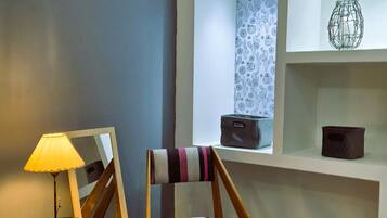 A modern living room with a striped rug, a wooden chair with a striped cushion, a lamp, and a shelf with decorative items.