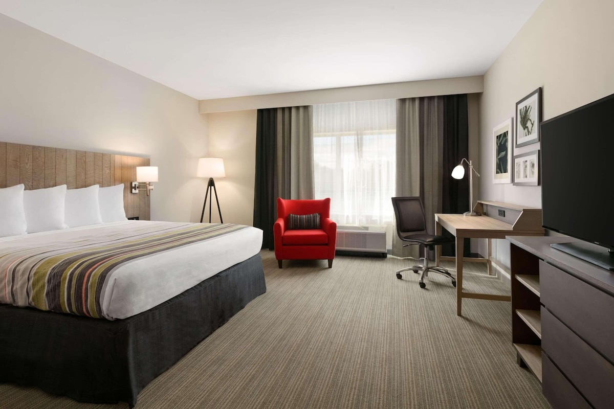A hotel room with a large bed, a desk, a red chair, a television, and a window with curtains.
