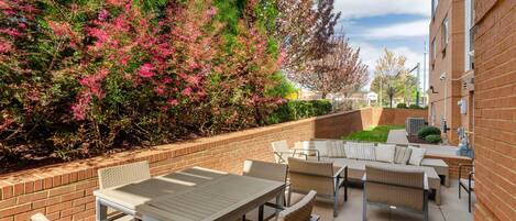 An outdoor patio area with tables and chairs, surrounded by a brick wall and lush greenery.