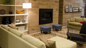 A living room with a brick wall, a flat-screen TV, a sofa, ottomans, and a coffee table. - Country Inn & Suites by Radisson, Charlottesville-UVA, VA (Charlottesville)