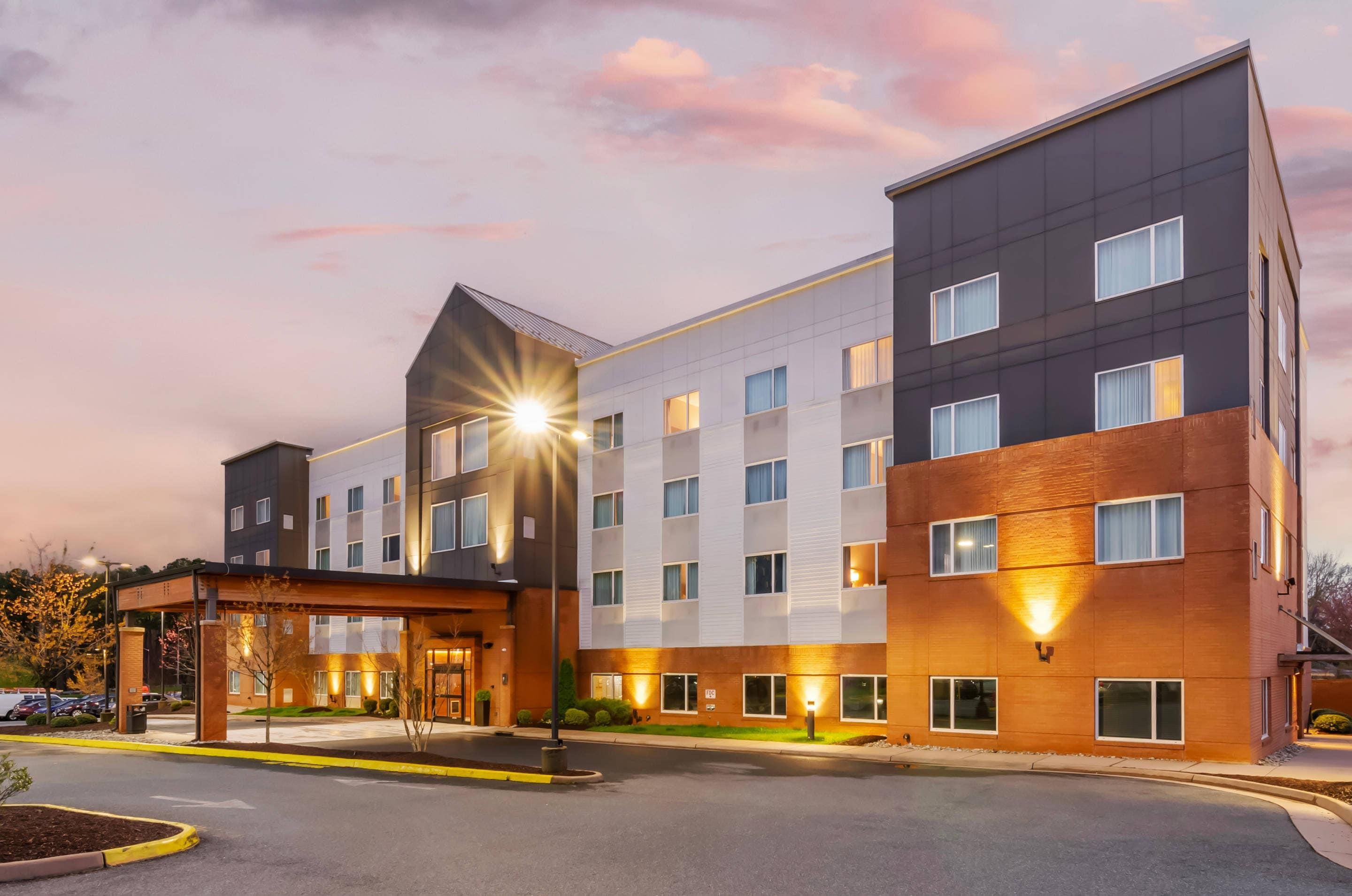 A multi-story hotel with a modern design, featuring a prominent entrance with a covered area and a parking lot in front.