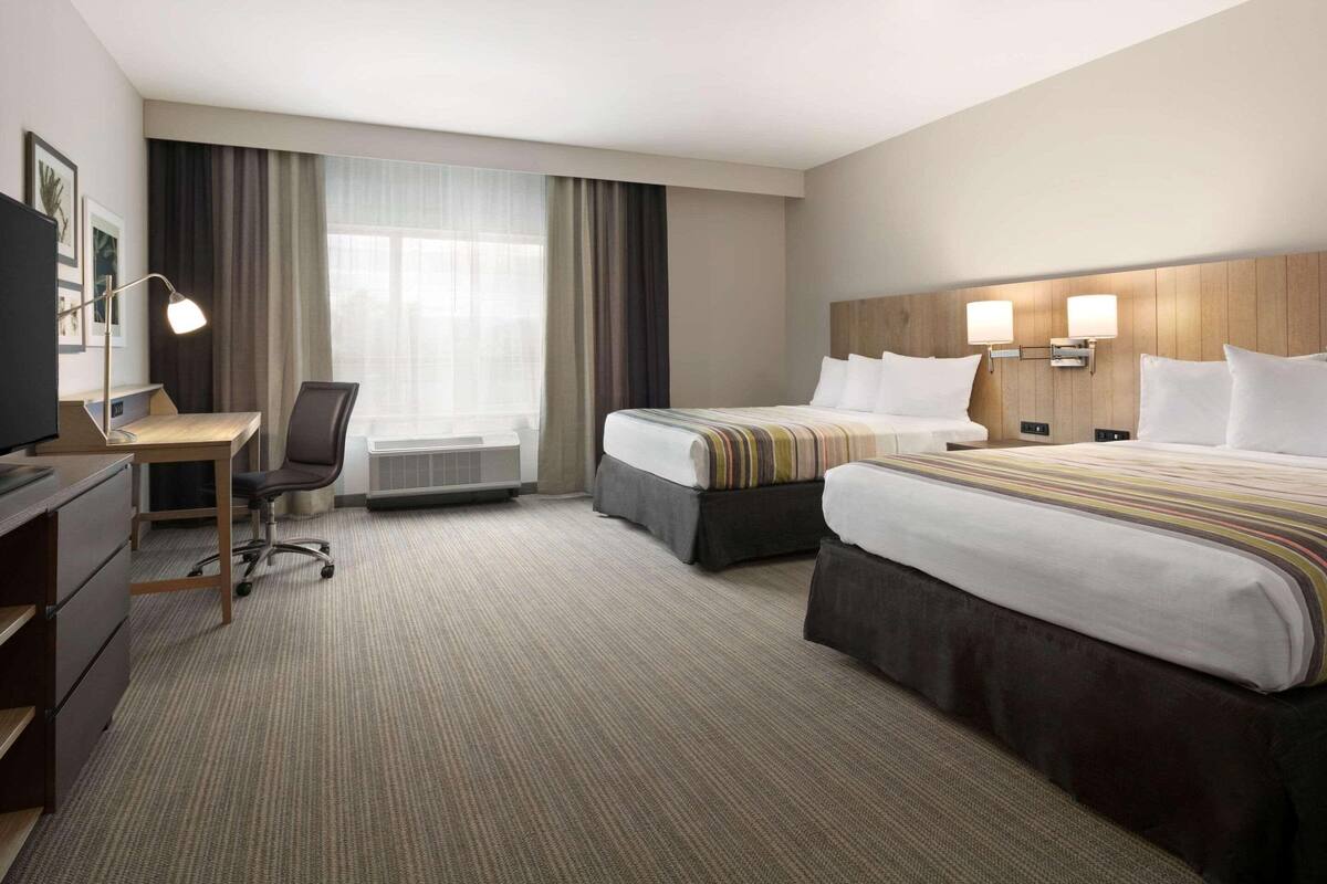 A hotel room with two beds, a desk, a chair, a TV, and a window with curtains.