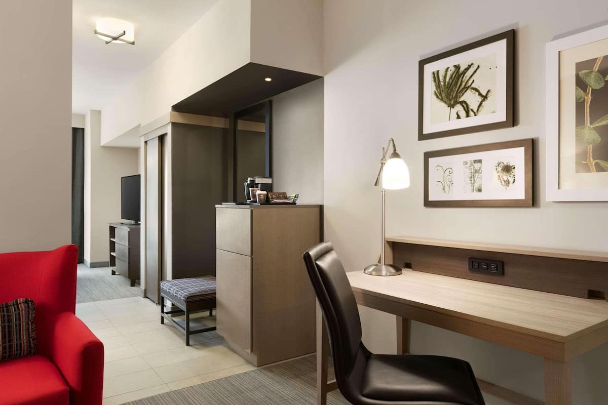 A modern hotel room with a desk, chair, red sofa, and artwork on the wall.