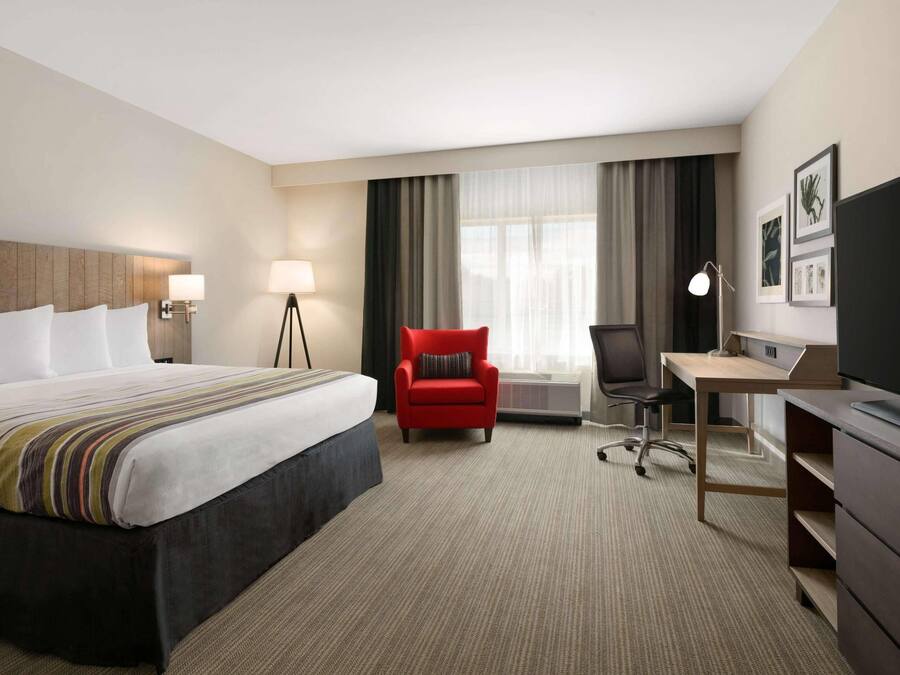 Een hotelkamer met een bed, een bureau, een stoel, een televisie en een raam met gordijnen.