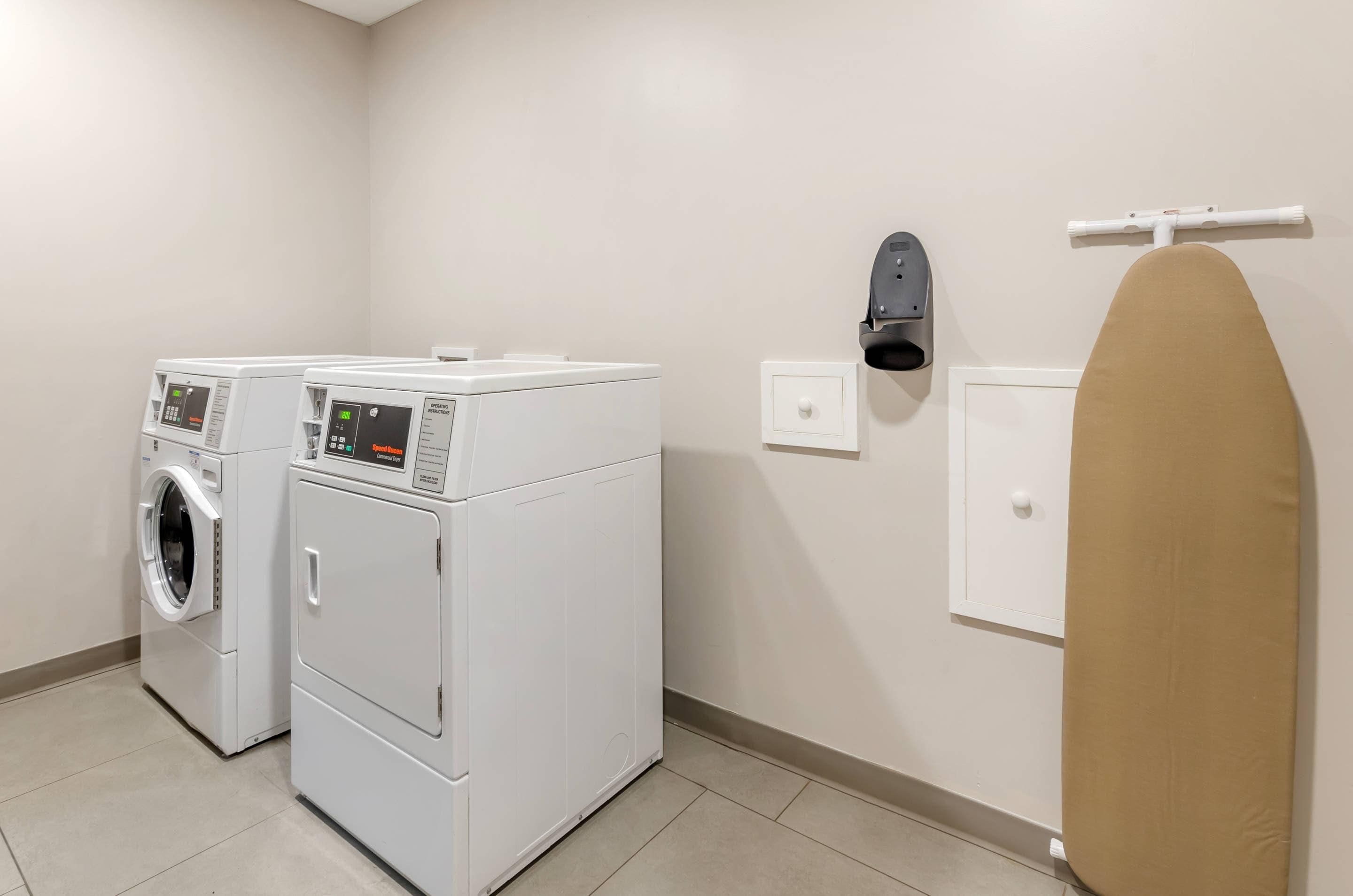 A laundry room with two stacked washers and dryers, a wall-mounted iron, and a small ironing board.