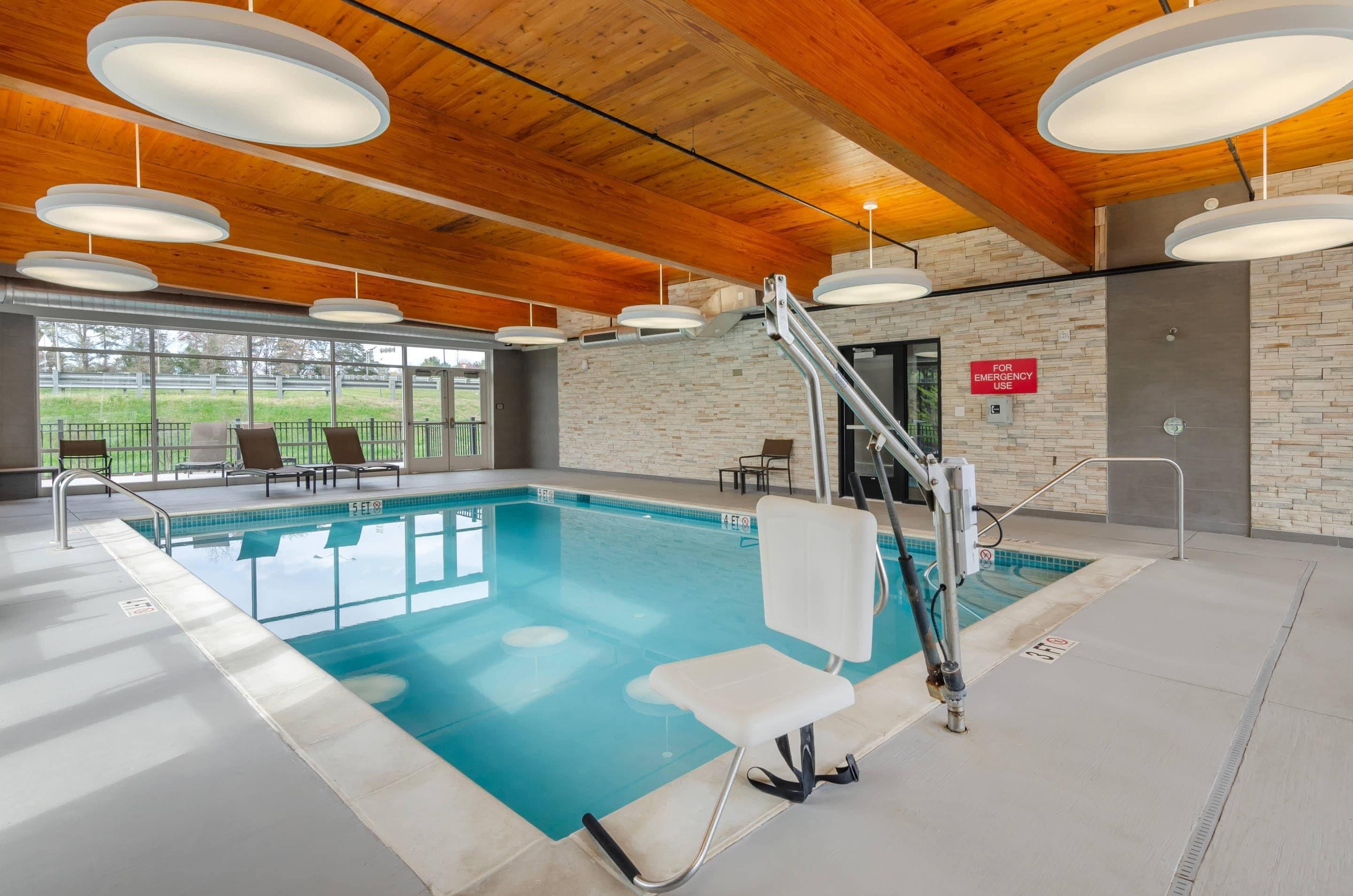 An indoor swimming pool with clear water, surrounded by lounge chairs and a wooden ceiling.