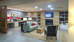 A modern living room with a sofa, coffee table, and TV. There is a fireplace, bookshelves, and a desk with lamps.