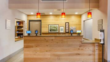 A reception desk with a wooden finish, a digital check-in kiosk, and a wall-mounted information board.