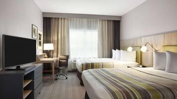 A hotel room with a bed, a desk with a TV, a chair, and a window with curtains.