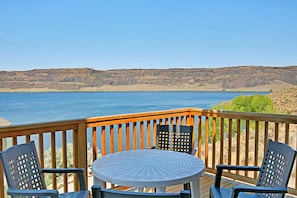 Una terraza con mesa y sillas que da a un cuerpo de agua y un paisaje montañoso.