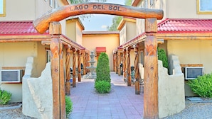 A wooden archway with the inscription "LAGO DEL SOL" leading to a building with multiple balconies and a central fountain.