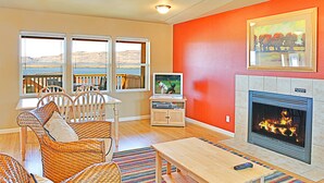A living room with wicker furniture, a fireplace, a television, and a view of a lake.