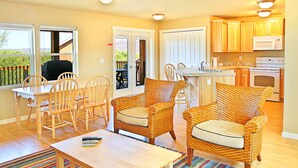 A cozy living room with wicker furniture, a dining area, and a kitchen with wooden cabinets and a microwave.