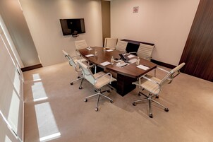 Una sala conferenze con un grande tavolo, sei sedie, un televisore a schermo piatto e un estintore.