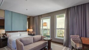 A hotel room with a bed, a sofa, a small table, a chair, and a window with curtains. - Hotel Cadoro Sao Paulo (São Paulo)