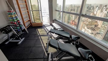 Una palestra con attrezzature per esercizi, una panca e vista sullo skyline urbano attraverso ampie vetrate.