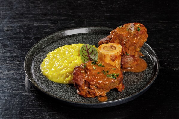 A plate with a meat dish, mashed potatoes, and a garnish on a dark plate.
